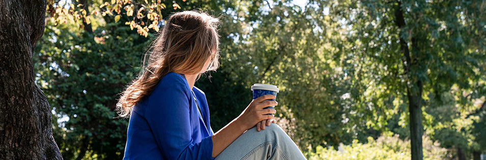 Person sitzt mit einem Becher in einem Park.