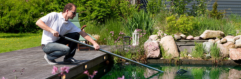 Person reinigt einen Gartenteich mit einem Kescher.