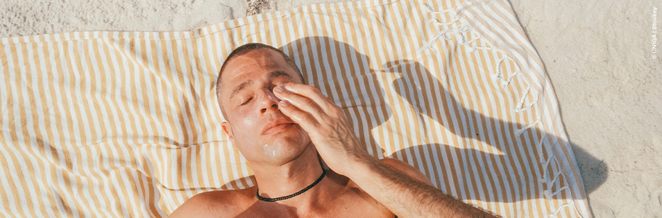 Mann liegt am Strand auf einem Badetuch