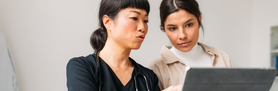 Zwei Personen betrachten gemeinsam die Anzeige eines Tablets. Eine Person zeigt auf den Bildschirm, die andere beobachtet die Inhalte.
