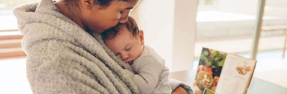 Person hält ein schlafendes Baby auf dem Arm in einem Innenraum.