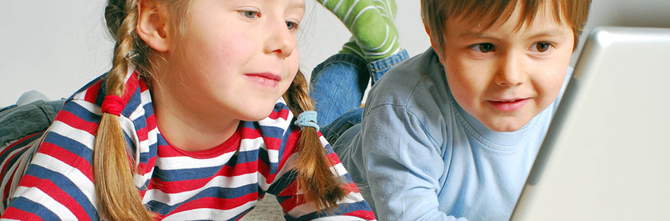 Zwei Kinder liegen vor einem Laptop und betrachten den Bildschirm.
