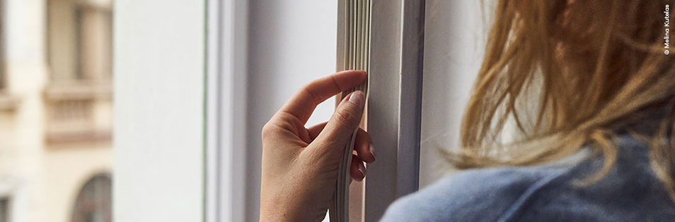 Person kontrolliert Fensterrahmen und Dichtung an einem geöffneten Fenster.