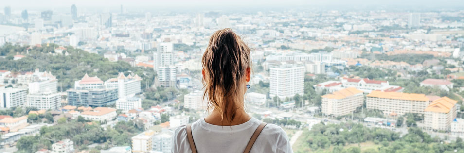 Person steht vor einem großen Fenster und blickt auf eine Stadtlandschaft. Symbolbild für Zukunftsplanung und private Pensionsvorsorge.