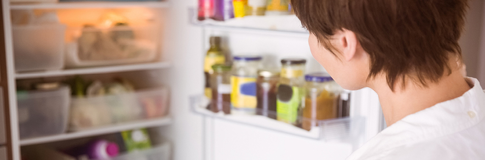 Person blickt in einen geöffneten Kühlschrank mit Lebensmitteln und Vorräten.