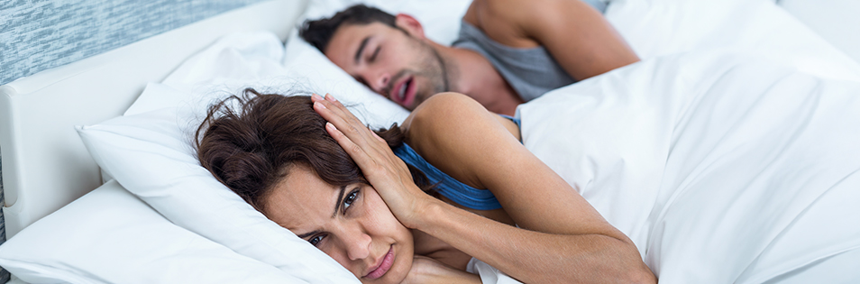 Schnarchender Mann im Bett - Frau hält sich die Ohren zu