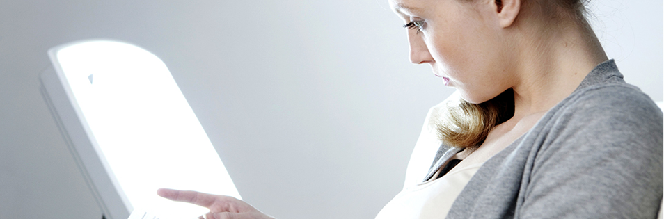 Person sitzt vor einer Lichttherapielampe zur Anwendung von Lichttherapie im Innenraum.