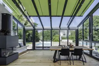 Wohnwintergarten mit grüner Markise und direktem Blick auf den Pool im Garten