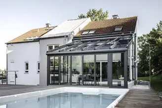 Außenansicht eines Wohnwintergartens mit großflächiger Glasfassade und Garten