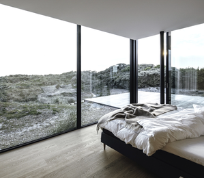 Rahmenlose Fenster im Schlafzimmer – freie Sicht in die Dünenlandschaft und nahtloser Übergang nach draußen