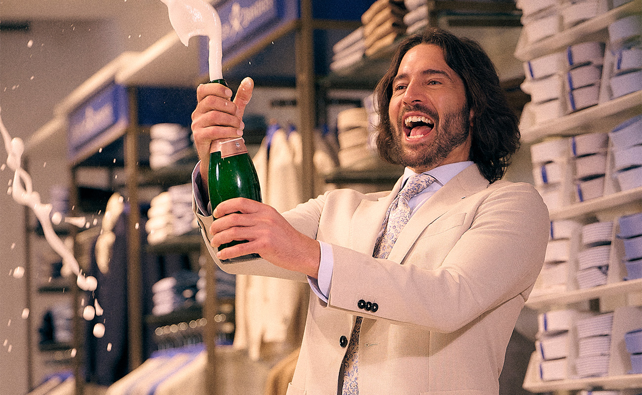 Model met beige trouwpak, opent fles champagne