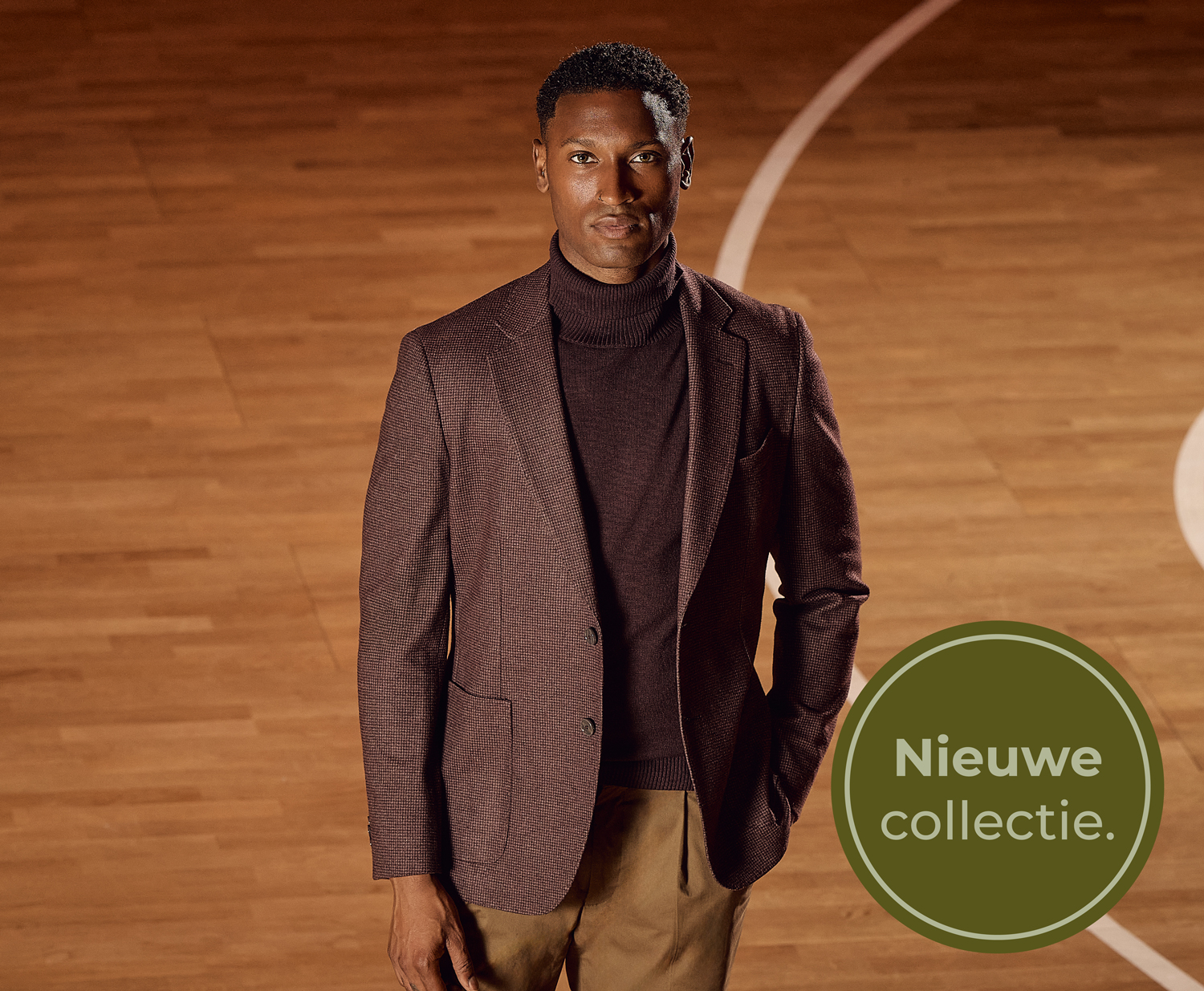 Man in a brown turtleneck and blazer stands on a wooden floor. A round badge reads "Nieuwe collectie" in the bottom right corner.