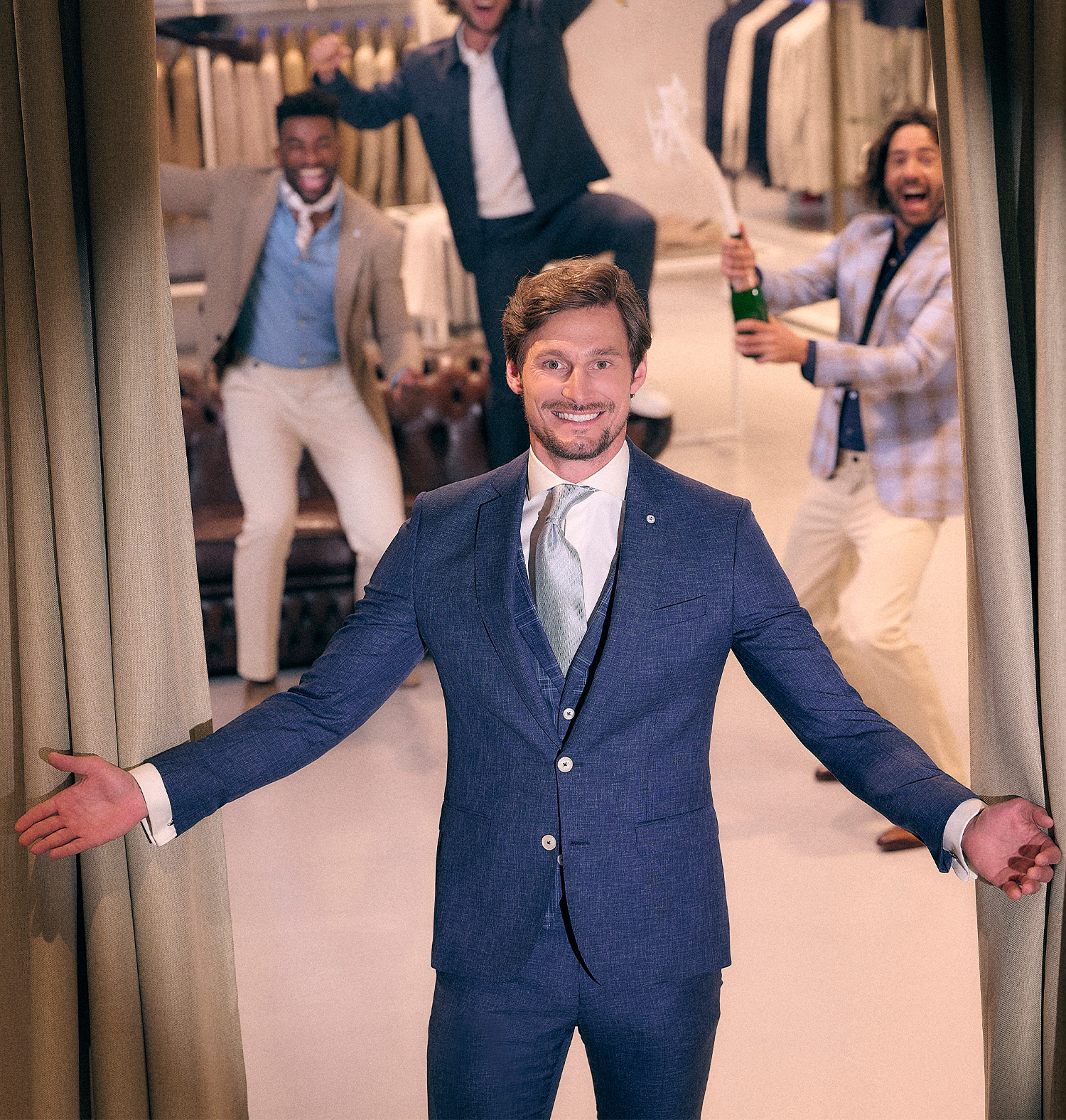 Model met open armen in een blauw trouwpak, op de achtergrond blije mannen