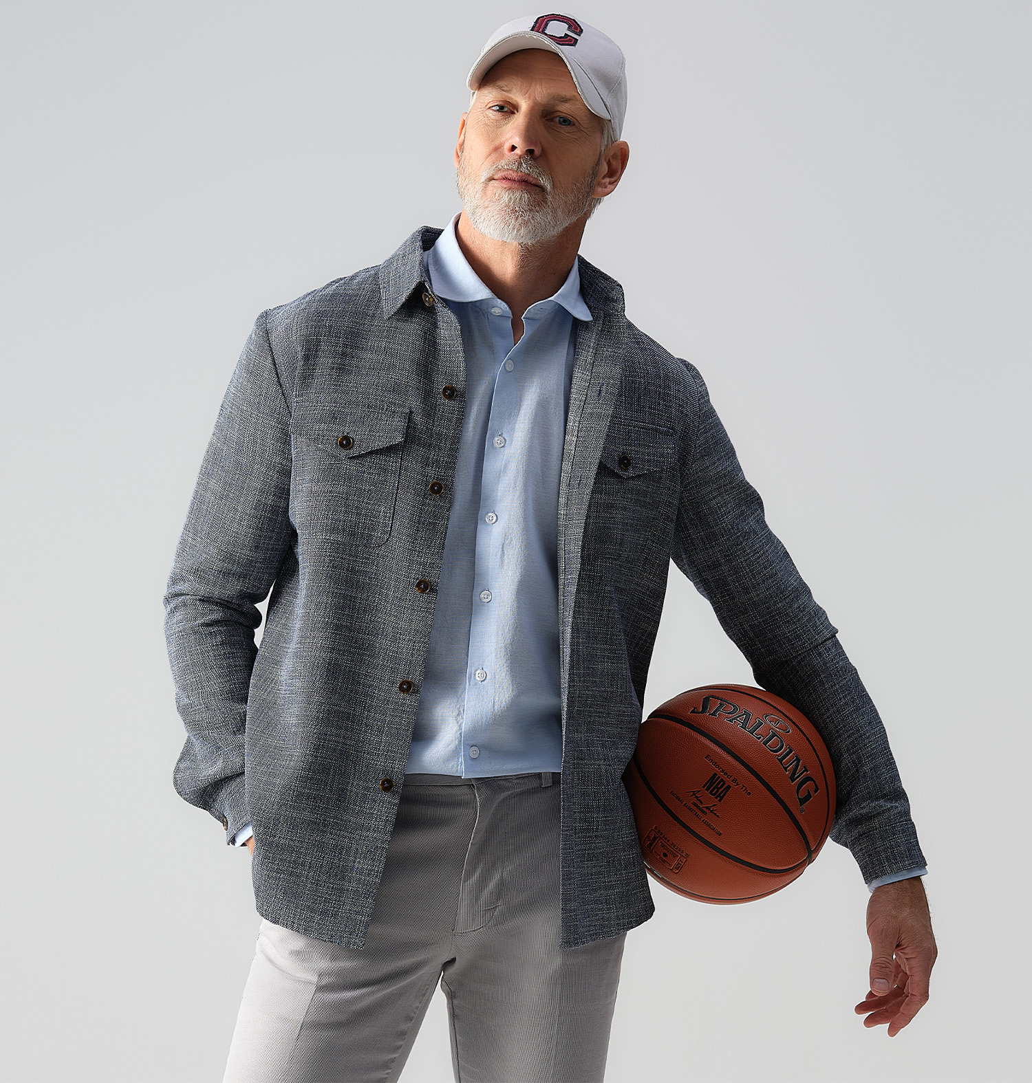 Man met een pet op en een grijze overshirt aan. Met een basketbal onder zijn arm.