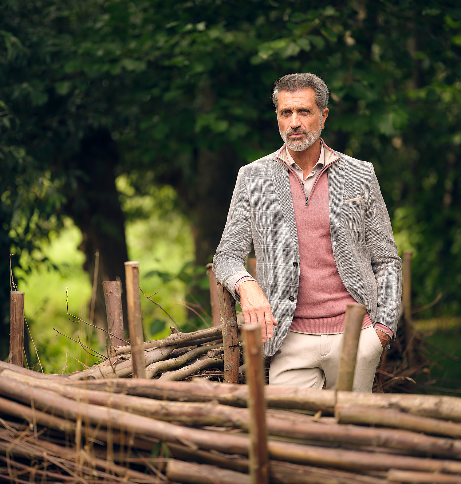 man gekleed in roze schipperstrui en geruit grijs colbert staand in het bos