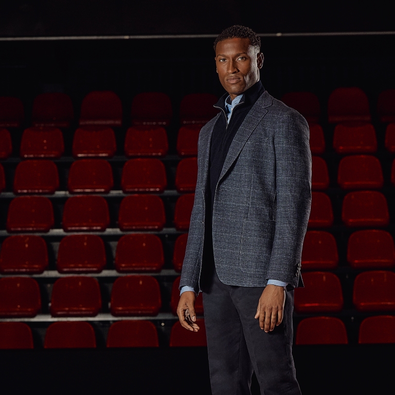 A man in a blue blazer stands confidently in front of empty red theater seats.
