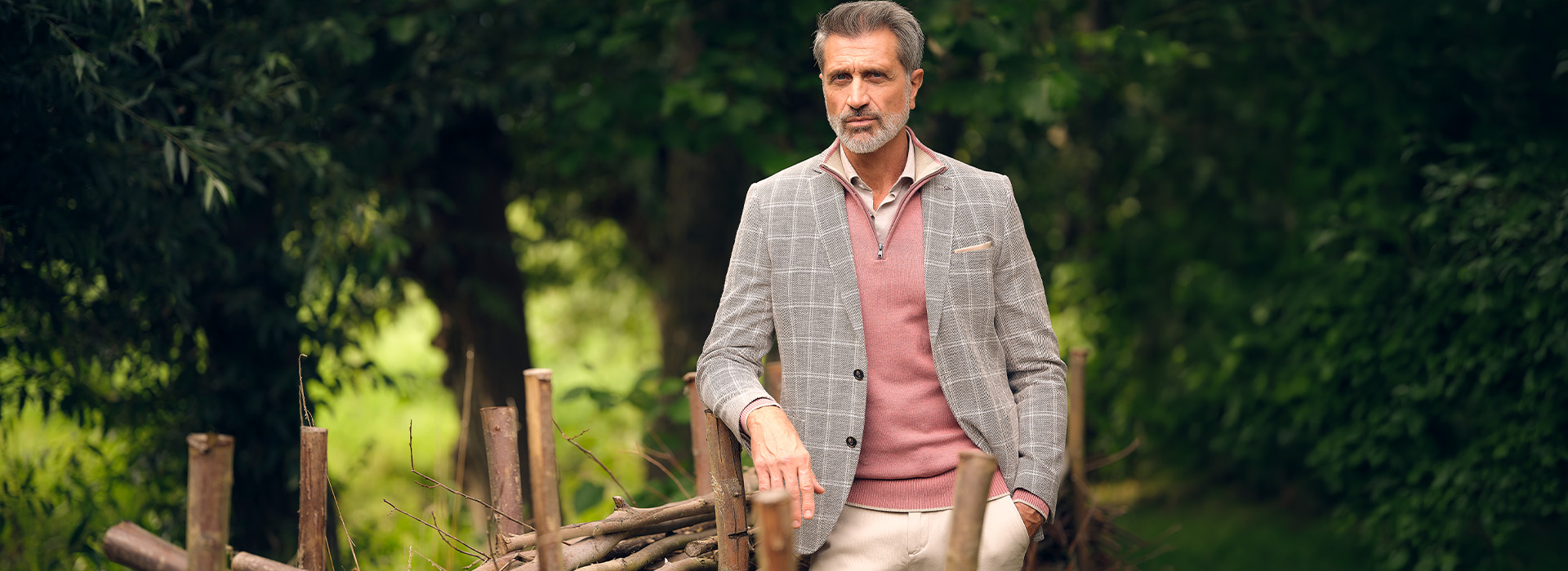 man gekleed in roze schipperstrui en geruit grijs colbert staand in het bos