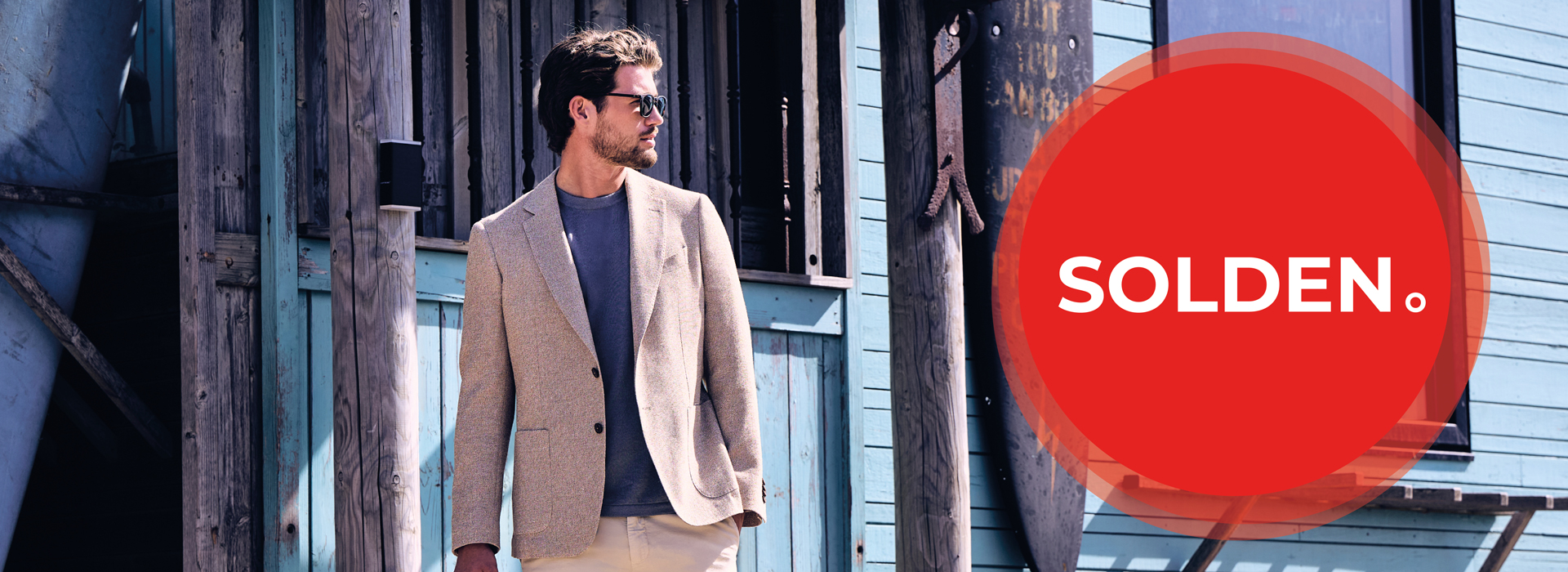 Man in beige blazer and sunglasses stands near a building; large red circle with "SOLDEN" text on the right.