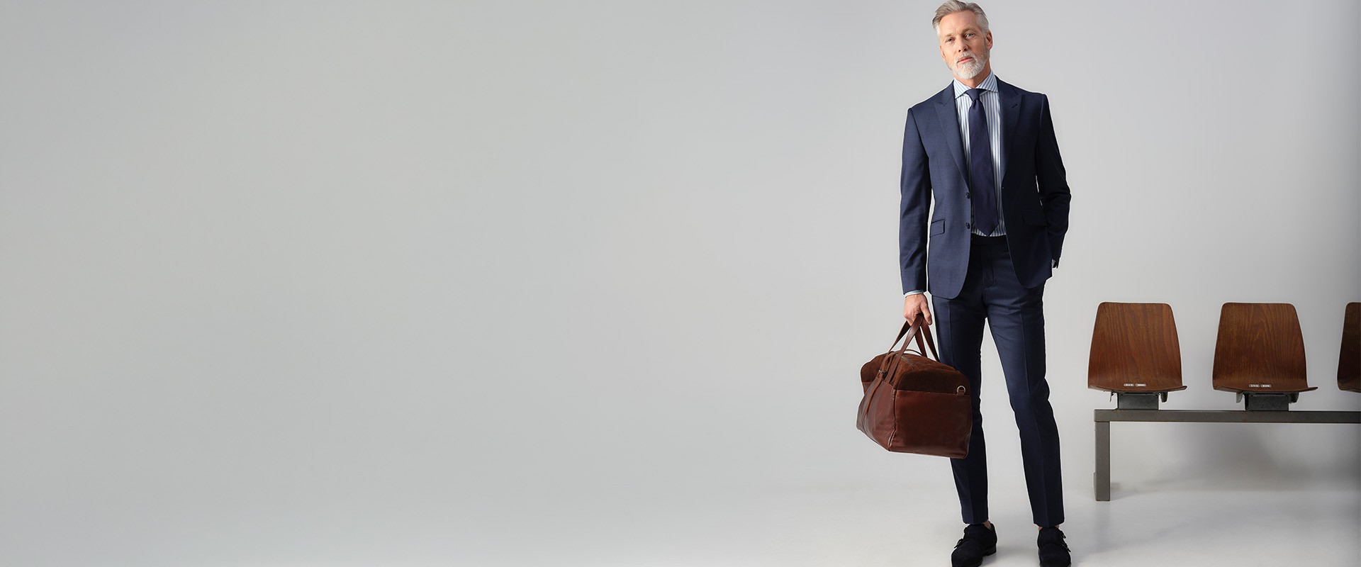 Man poserend in pak in een fotostudio met een sporttas vast