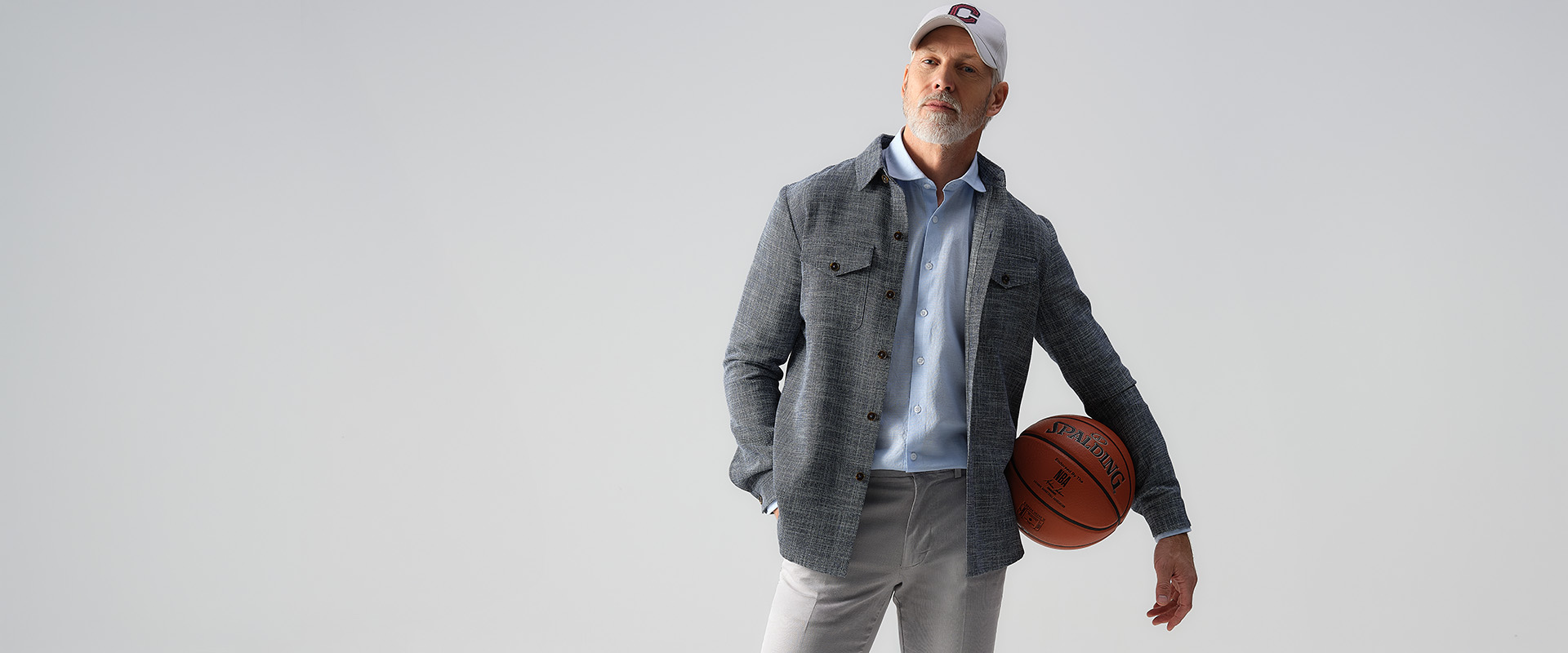 Man met een pet op en een grijze overshirt aan. Met een basketbal onder zijn arm.