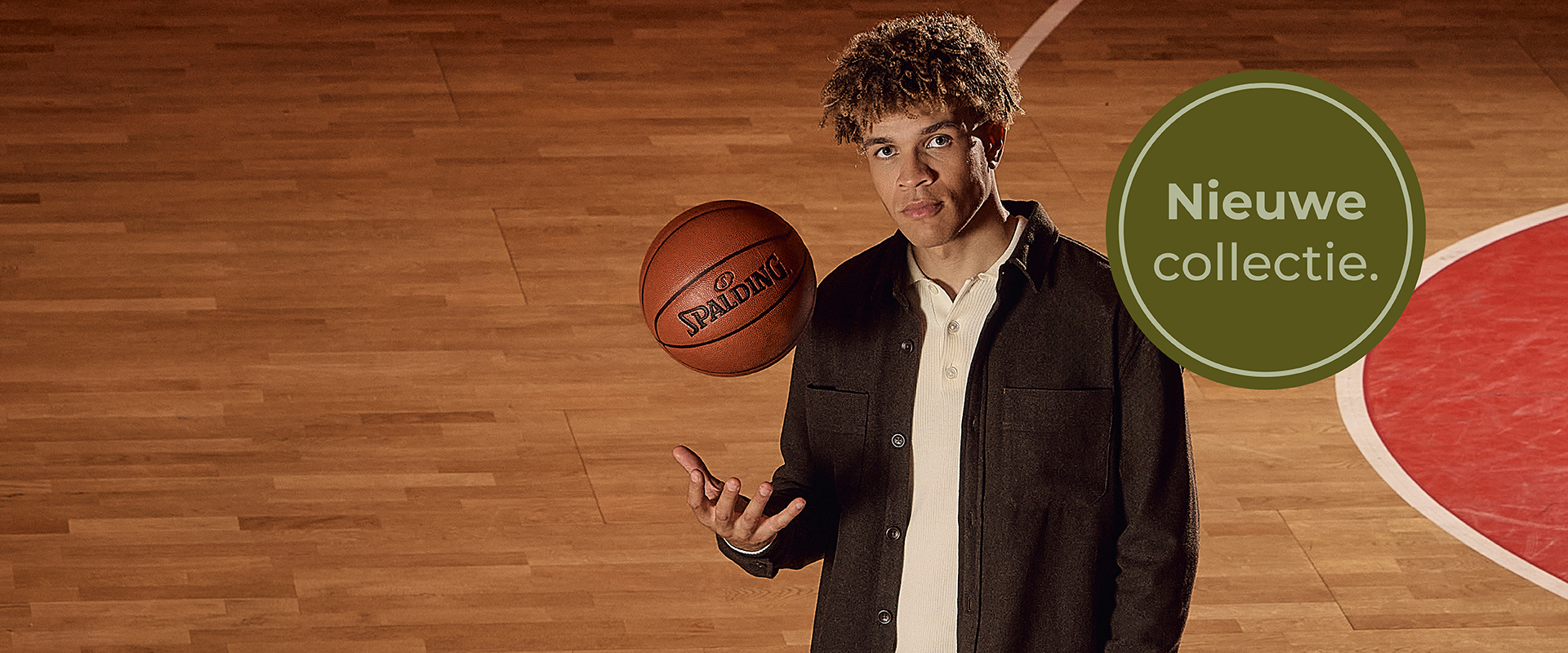 Man standing on a basketball court, holding a ball. Circular banner says "Nieuwe collectie" in Dutch.