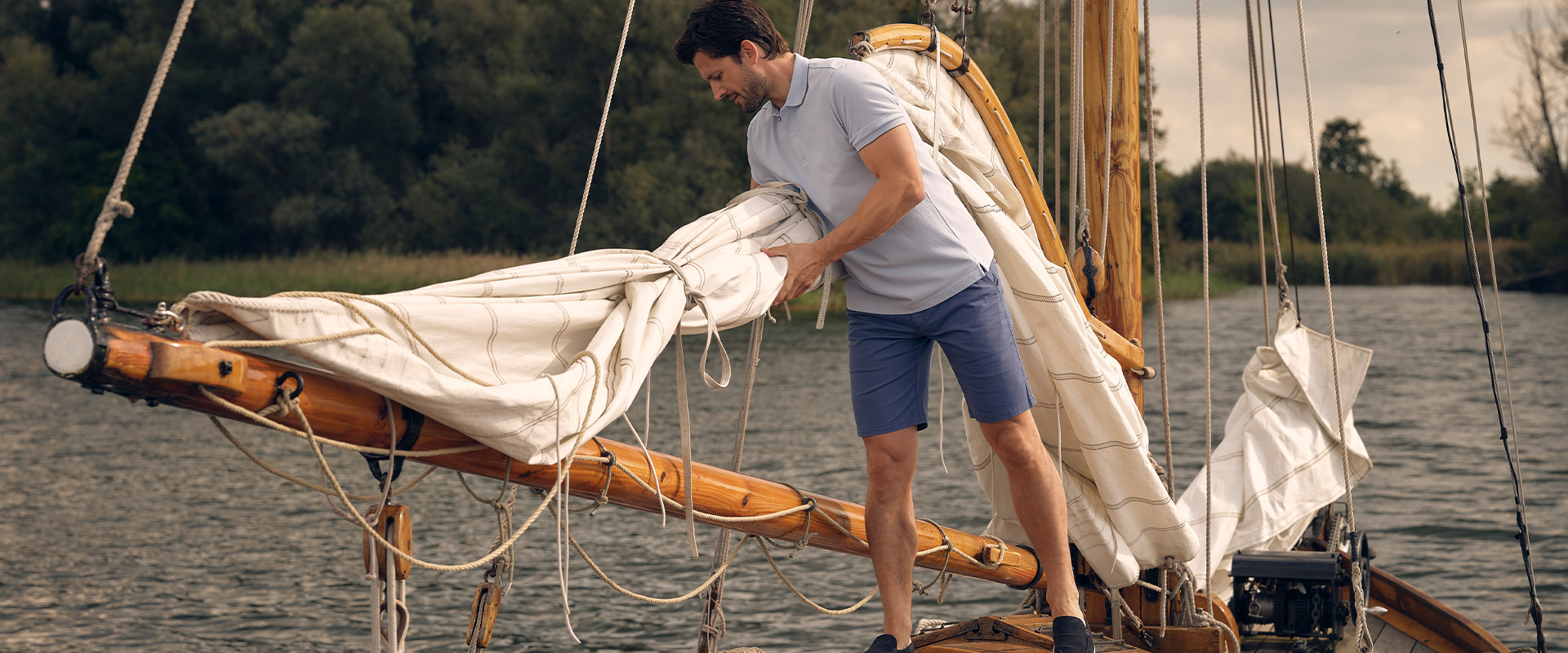 Man op een zeilboot leunend over de vlaggenmast