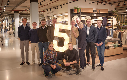 Teamfoto waarvan 2 mannen een lichtgevende 5 vasthouden ivm 5-jarig jubileum