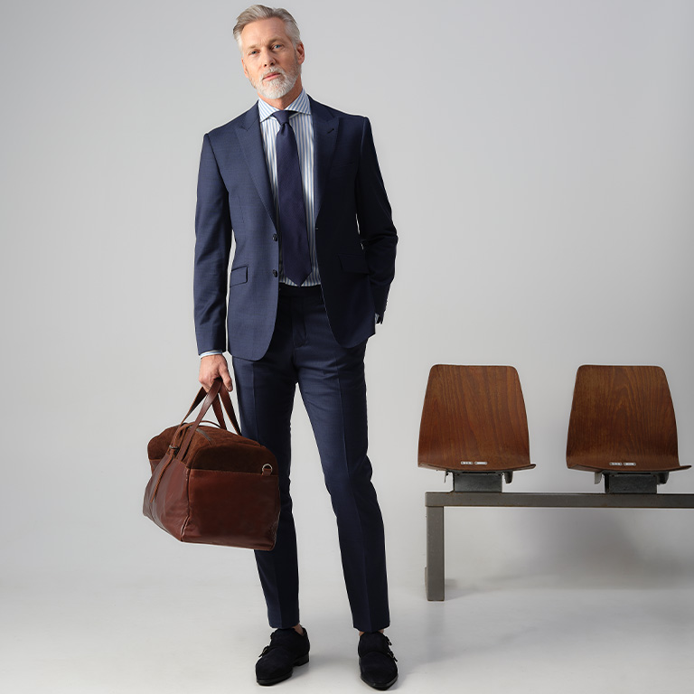 staande man in een blauw pak met een gymtas vast