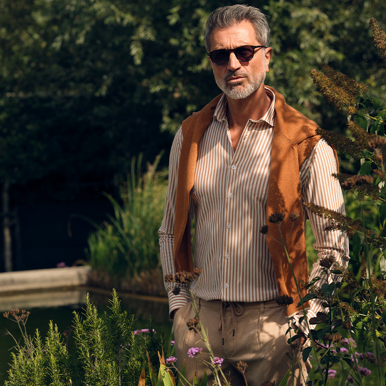 Man met kleding van hetmerk campbell aan poserend voor een vijver tussen planten