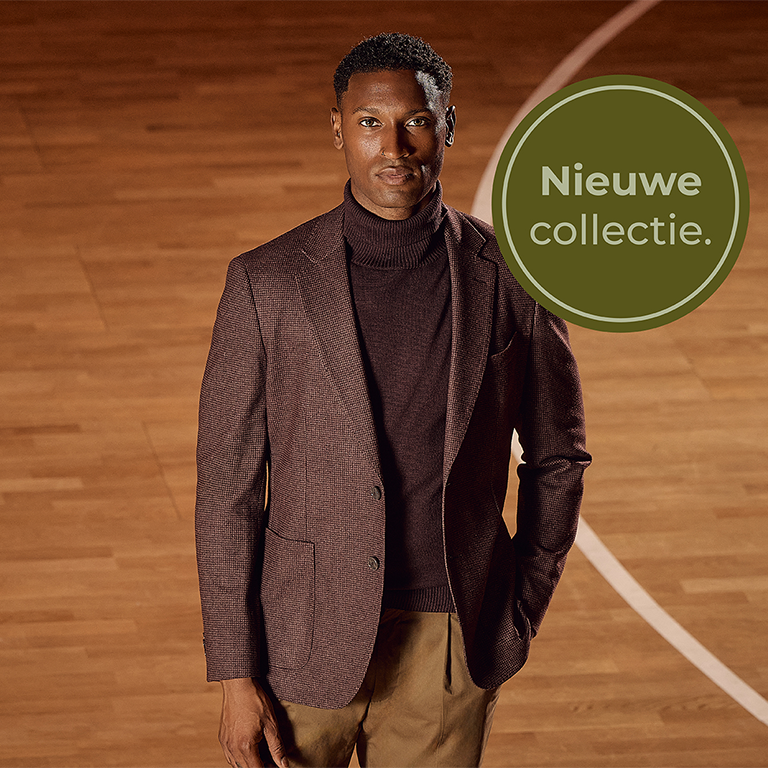 Man in a dark brown suit jacket and turtleneck stands on a wooden floor. A green circle reads "Nieuwe collectie" in Dutch, meaning "New collection."