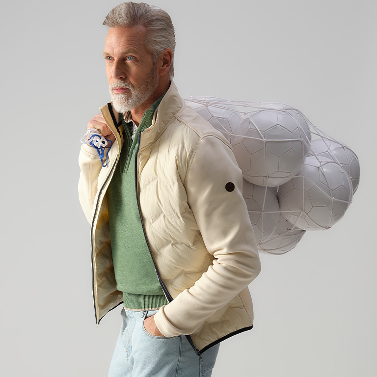 Man met een wit vest aan en draagt een zak voetbal-ballen op zijn rug