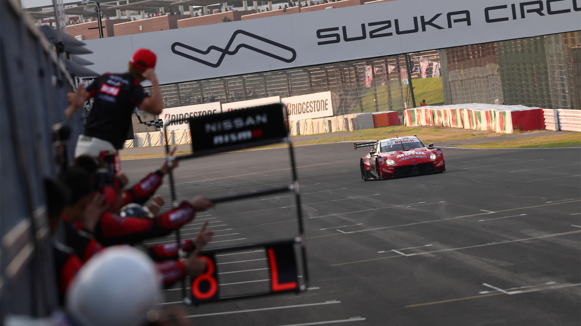 Nismo team members hold out a pit board and celebrate as the winning #23 car crosses the line