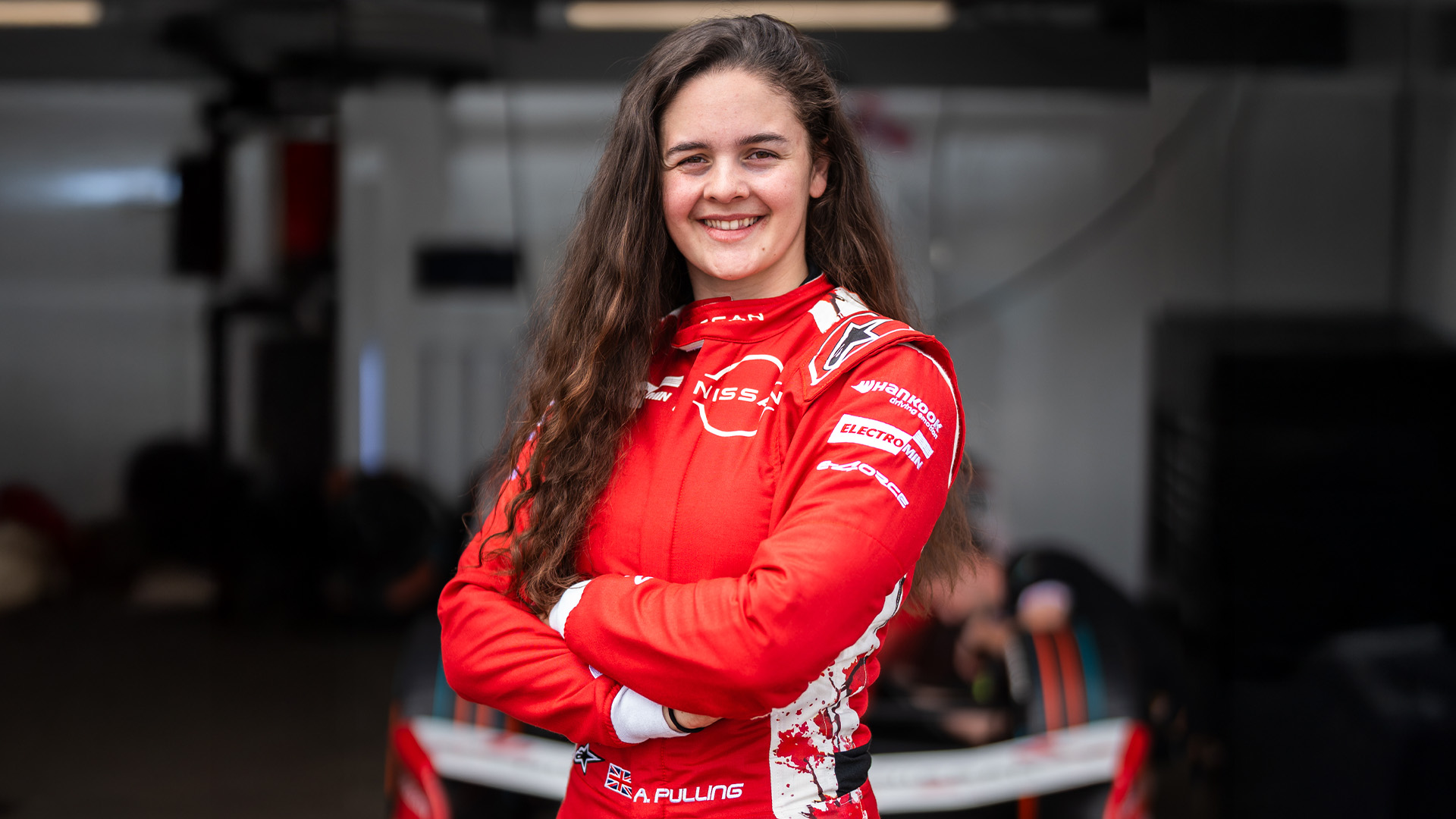 Abbi Pulling smiles for the camera. She is wearing her red Nissan race suit and has her arms folded