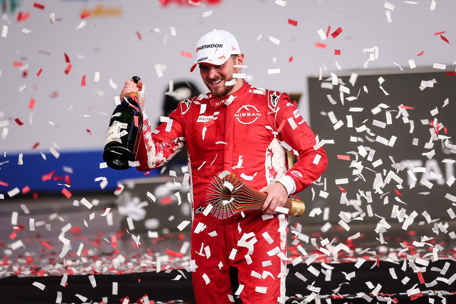 Oliver Rowland on the podium, trophy in one hand and champagne bottle in the other as red and white confetti falls around him
