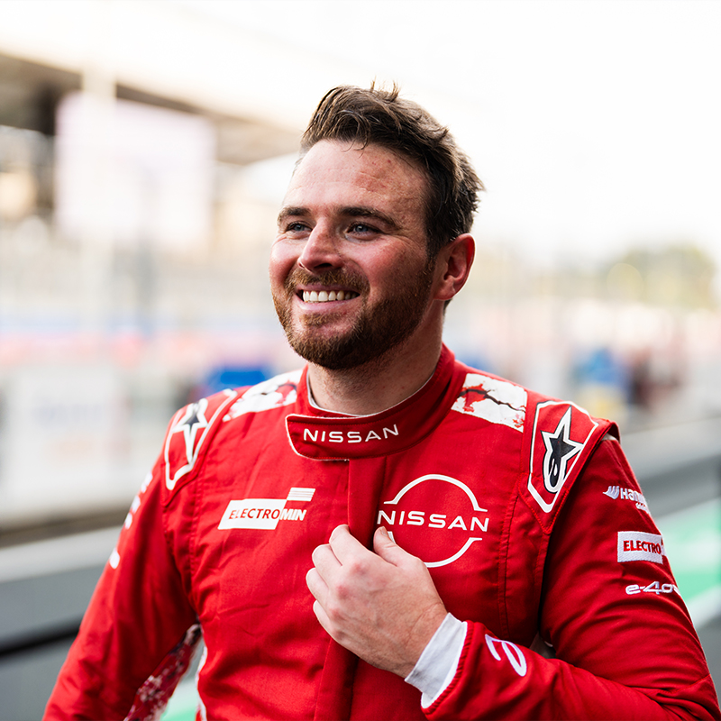 Oliver Rowland smiling after a race, wearing his red Nissan Formula E race suit