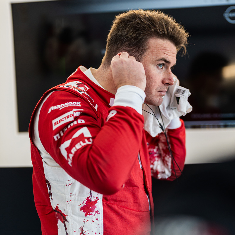 Oliver Rowland puts his earplugs in while wearing his red race suit in the Nissan Formula E Team garage