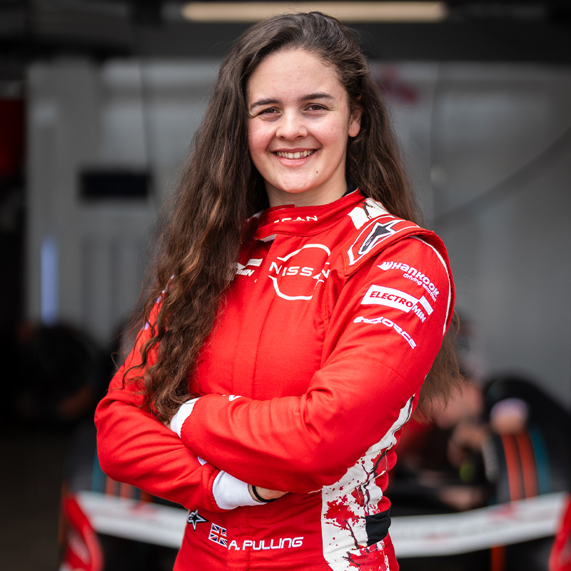 Abbi Pulling smiles for the camera. She is wearing her red Nissan race suit and has her arms folded
