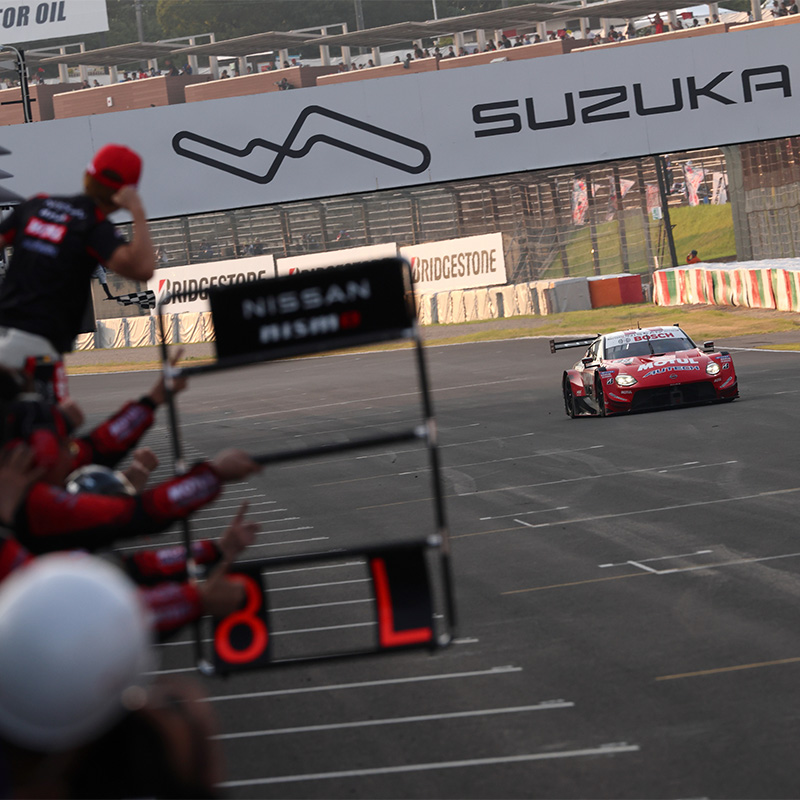 Nismo team members hold out a pit board and celebrate as the winning #23 car crosses the line