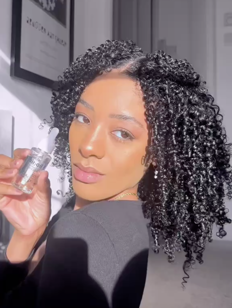 A lady with curly black hair with the Miracle Hair Oil