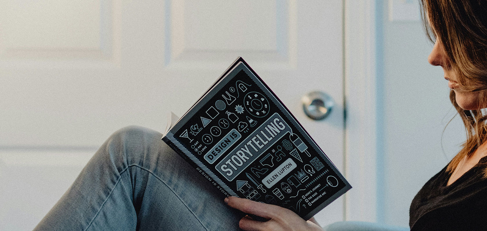 Person, die in einem sanft beleuchteten Raum mit einer weißen Tür im Hintergrund sitzt und ein Buch mit dem Titel „Storytelling“ liest.