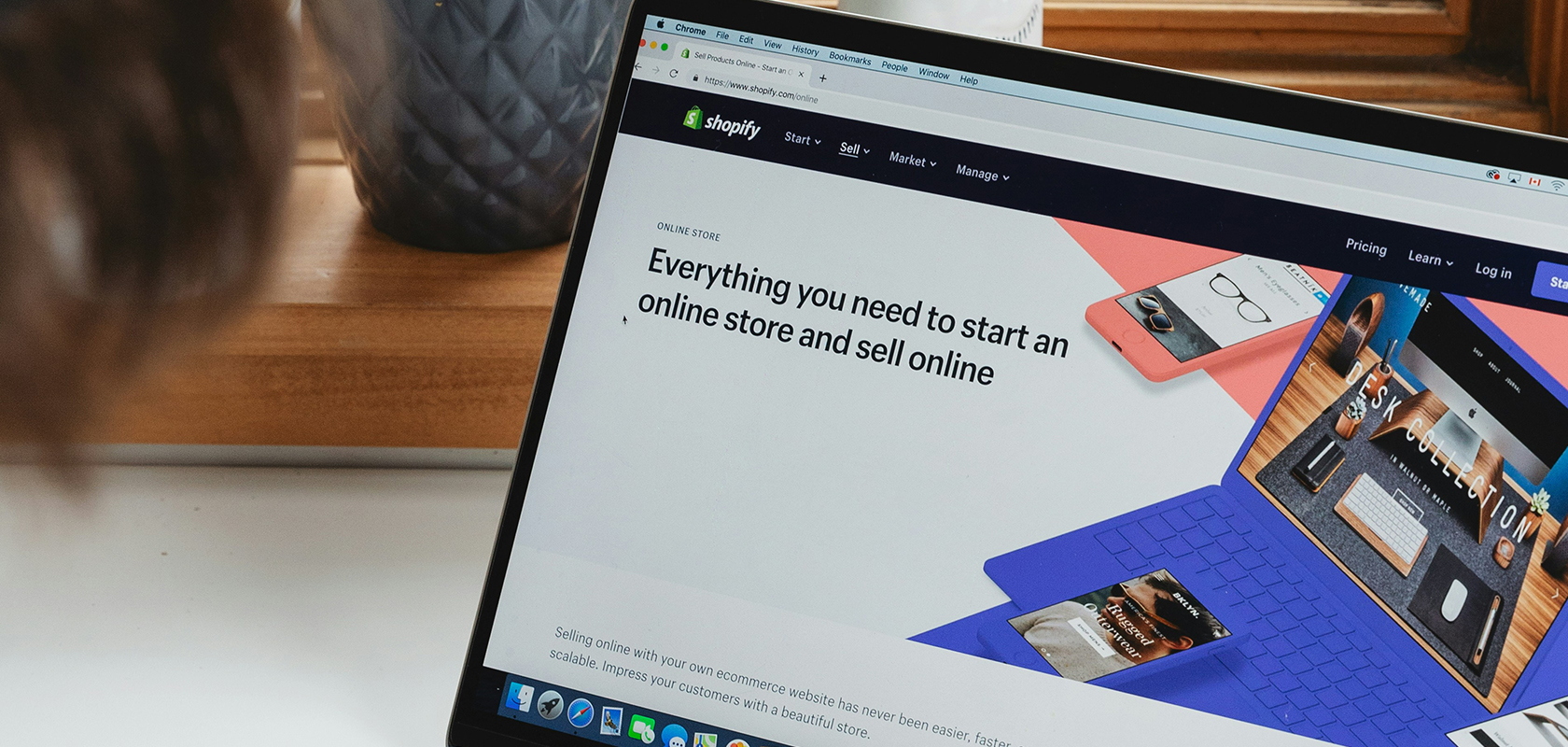 Laptop on desk showing Shopify webpage "Everything you need to start an online store", blurred person at left and potted plant behind.