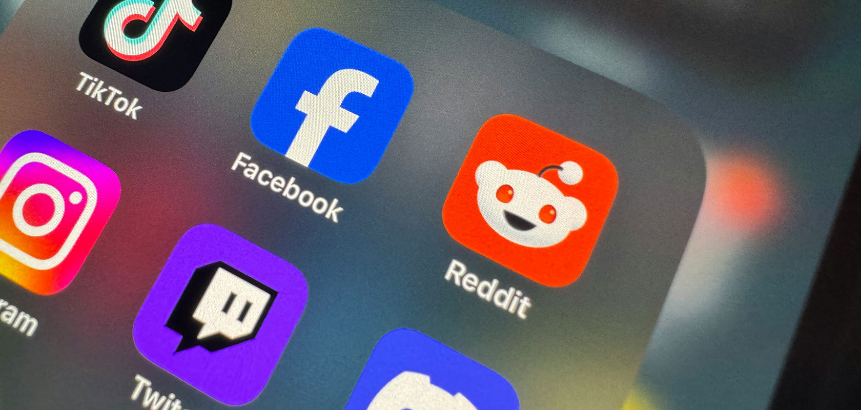 Nahaufnahme des Smartphone-Startbildschirms mit Symbolen für soziale Apps: TikTok, Facebook, Reddit, Instagram, Twitch.