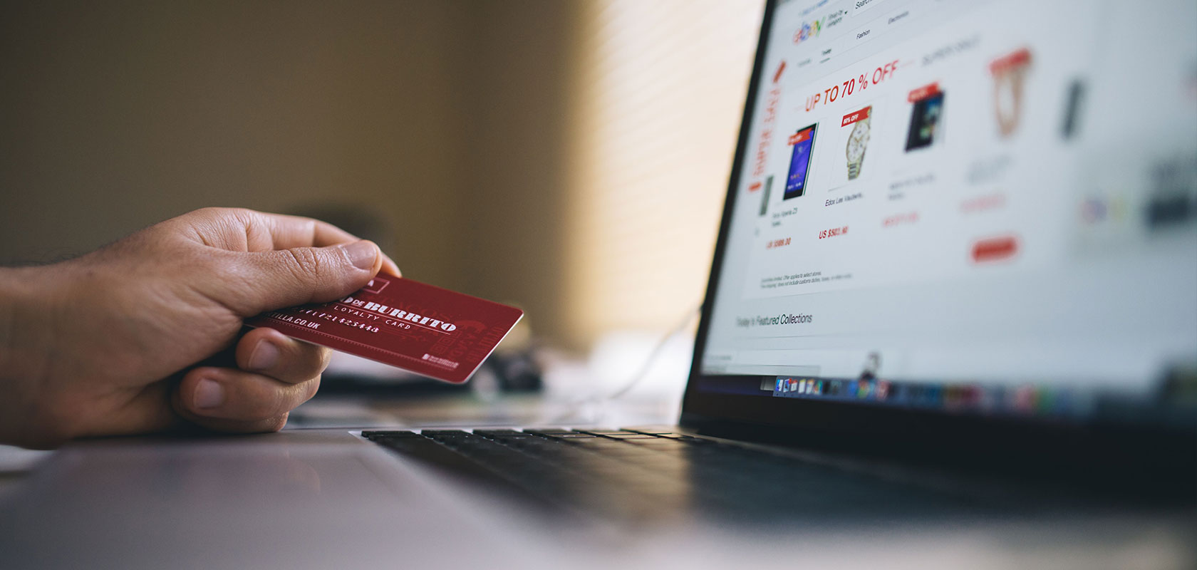 Person hält eine Karte beim Online-Shopping am Laptop.