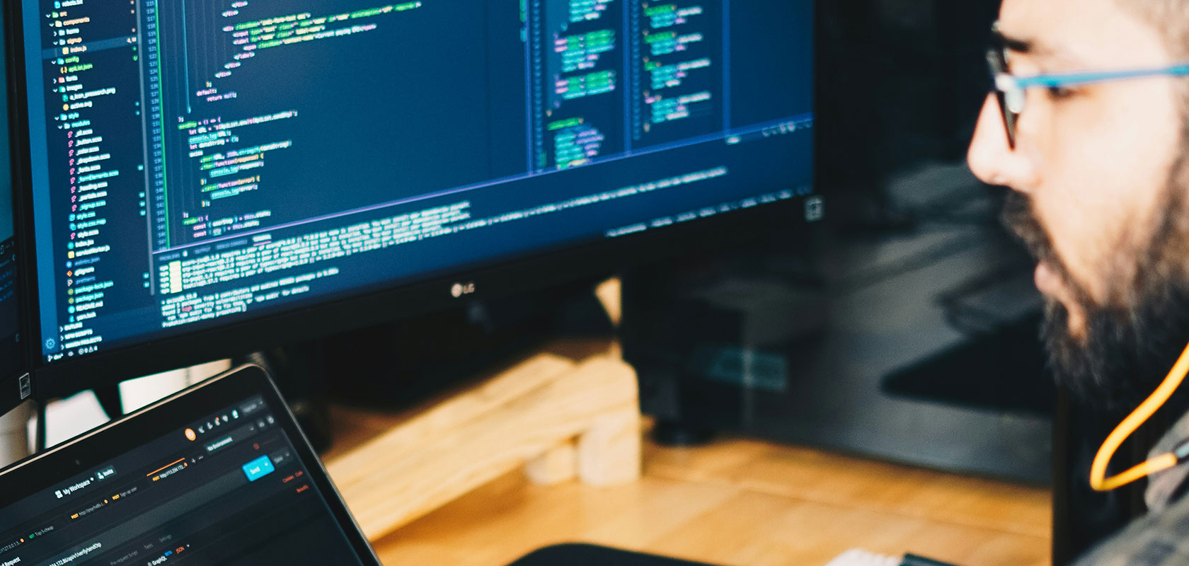 Eine Person, die an mehreren Computerbildschirmen arbeitet, auf denen Code angezeigt wird, mit unscharfem Gesicht und Lichtreflexen.