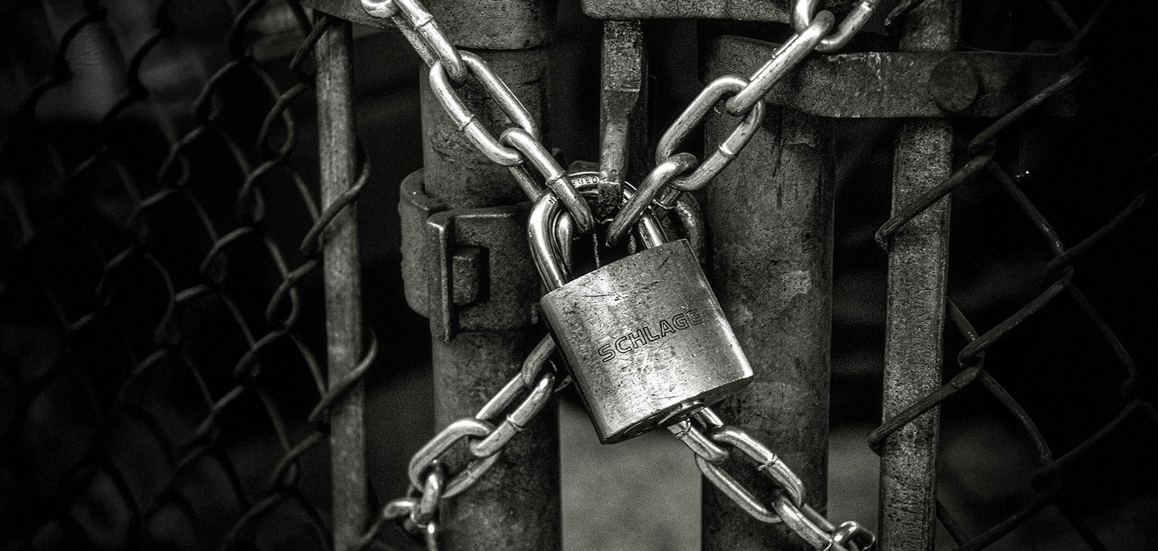 Eine schwere Kette mit einem Vorhängeschloss sichert ein Metalltor und vermittelt Sicherheit und Geschlossenheit.