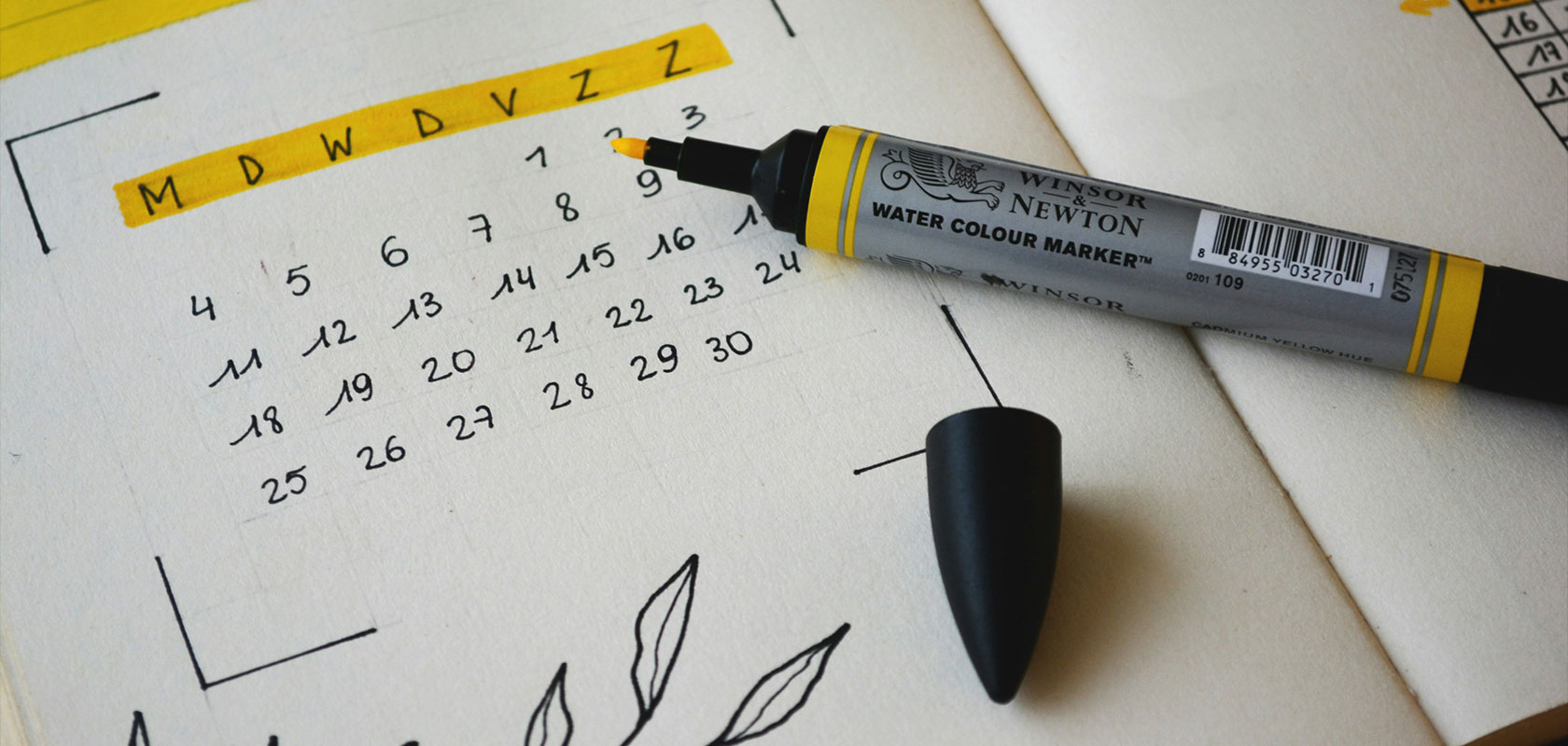 Offener Planer mit einem handgezeichneten Kalender, hervorgehobener Woche und einem gelben Wasserfarbenmarker mit abgenommener Kappe.