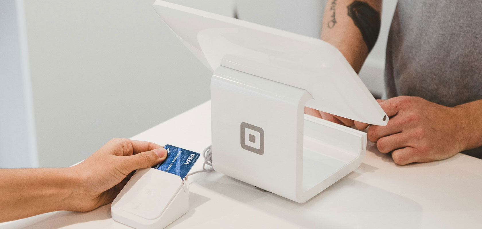 Customer holds blue credit card to card reader beside a white Square point-of-sale terminal.