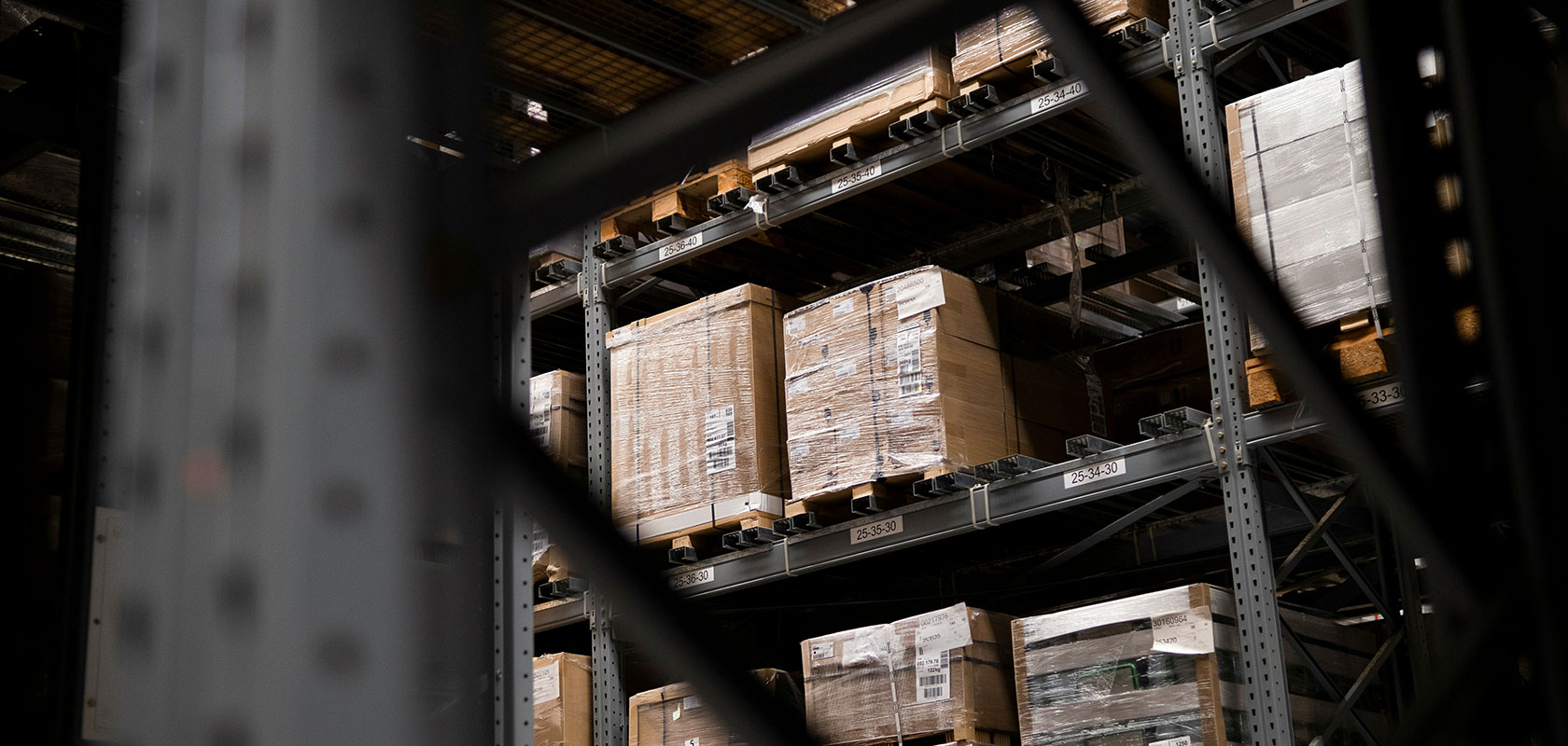 Blick auf Lagerregale, die mit großen, verpackten Paletten gefüllt sind und von Metallträgern umgeben sind.