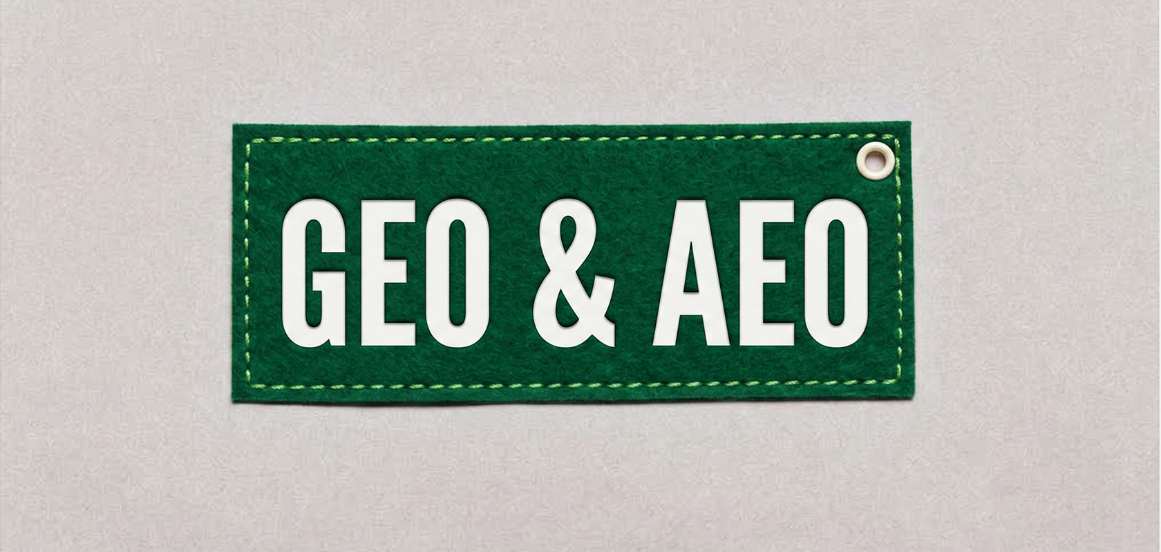 Grünes, rechteckiges Etikett mit weißem Schriftzug „GEO & AEO“ und einer Metallöse in der rechten oberen Ecke vor grauem Hintergrund.