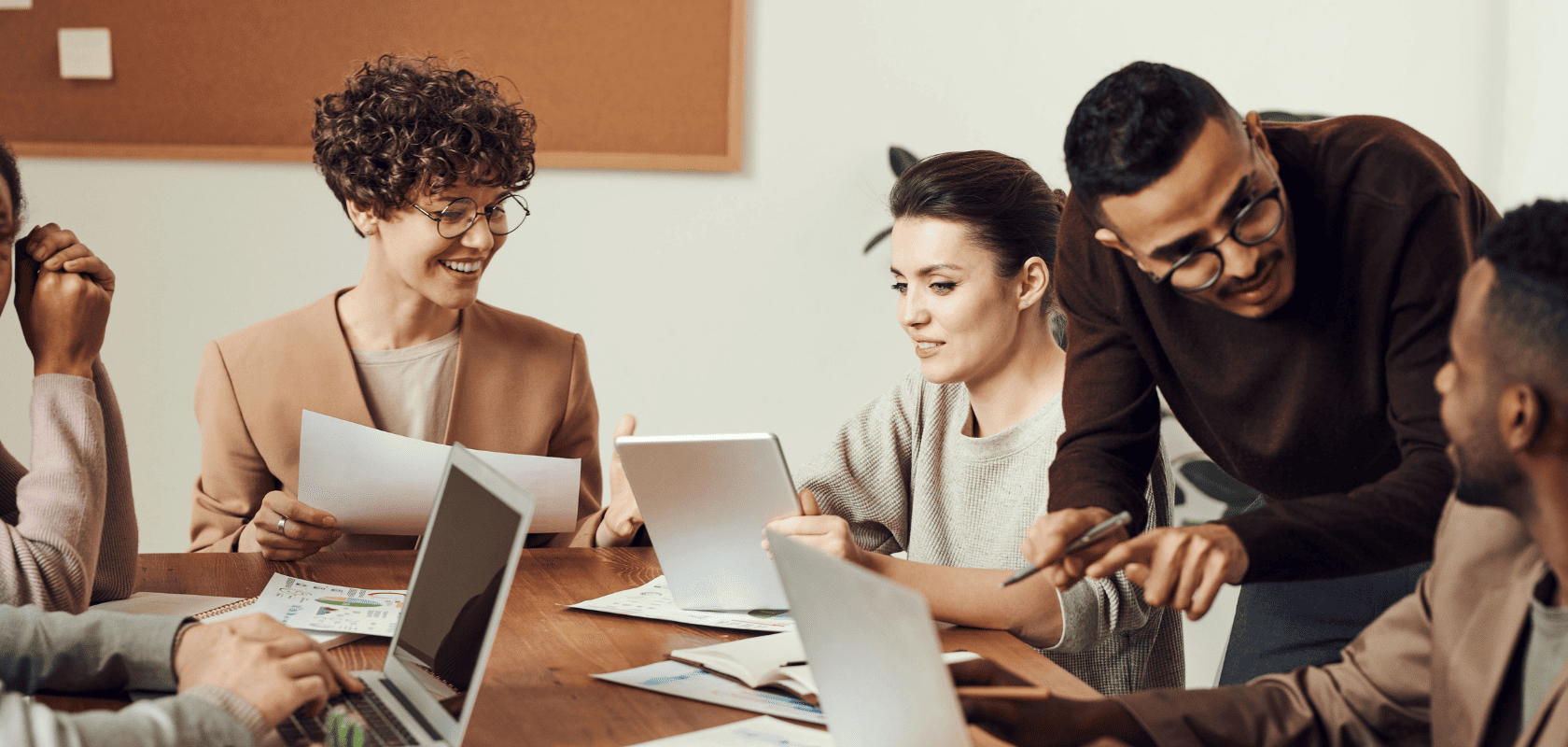 Eine Gruppe von Personen in einem Besprechungsraum, die mit Laptops und Dokumenten auf einem Holztisch arbeiten und diskutieren.